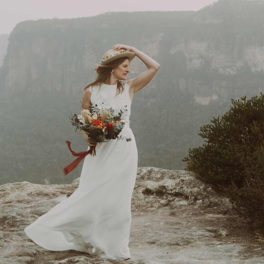 Woman in a white dress with a bouquet standing on a mountainous landscape