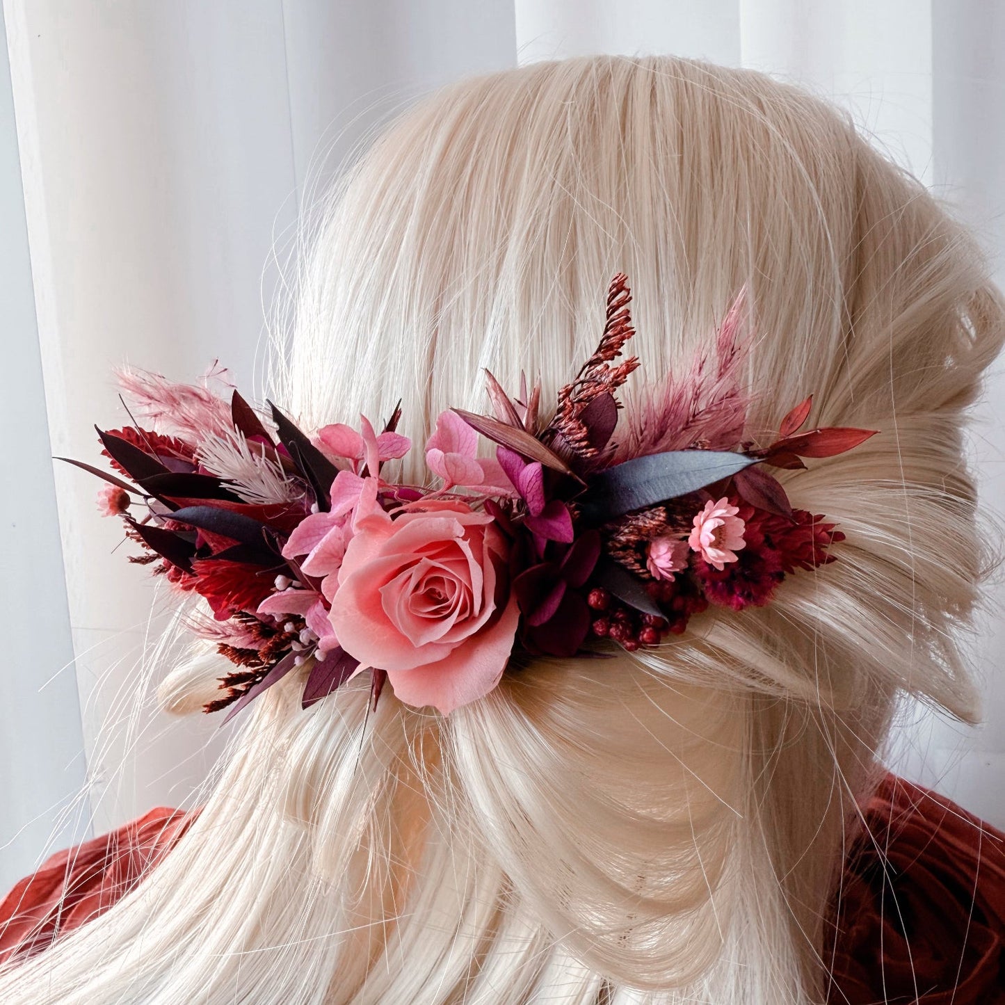 Elegant wedding hairpiece featuring coral pink preserved rose, burgundy leaves, and dried flower arrangement for boho bride hairstyle