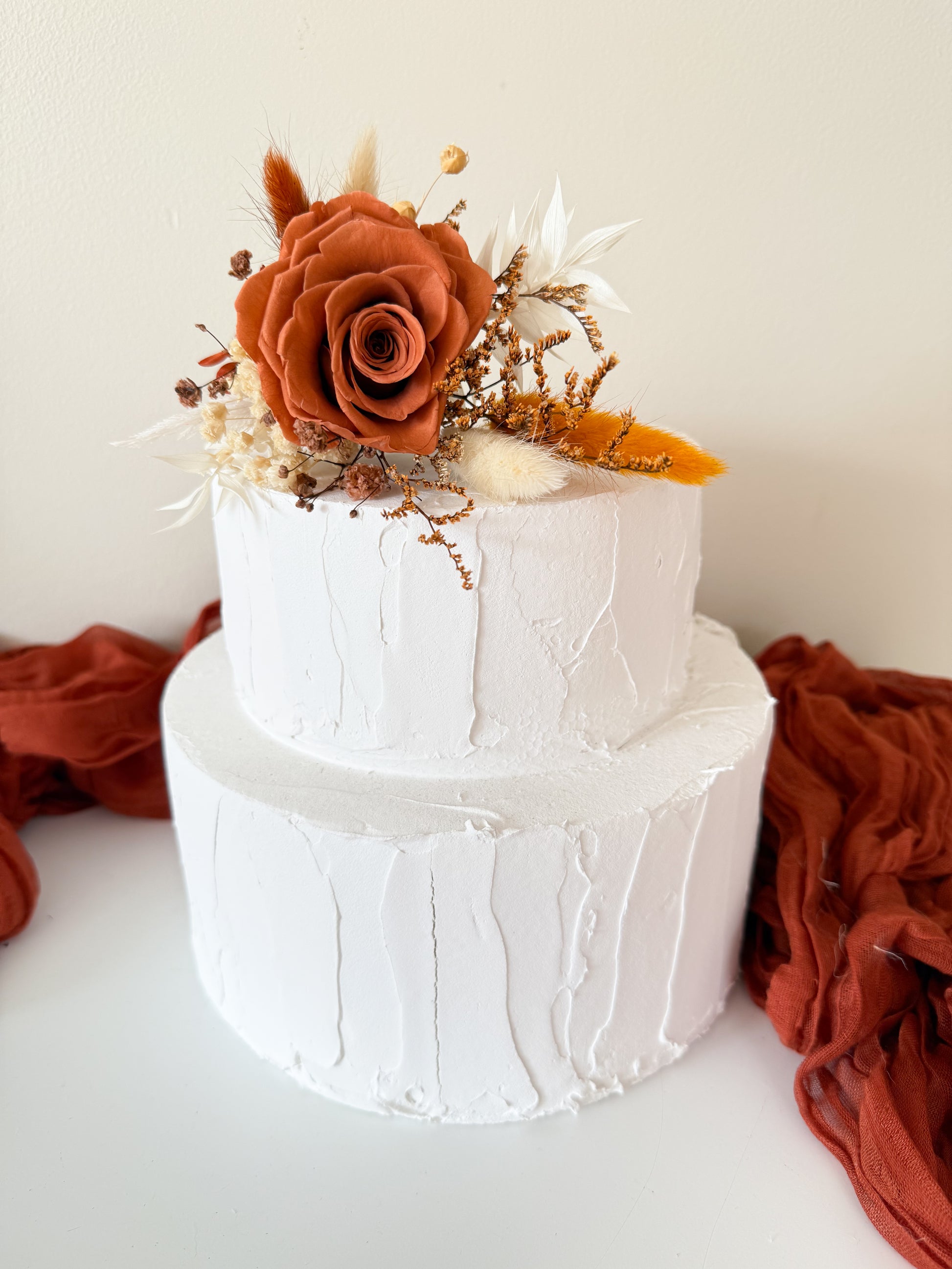 Two-tier white cake decorated with dried terracotta flower topper and rust silk fabric