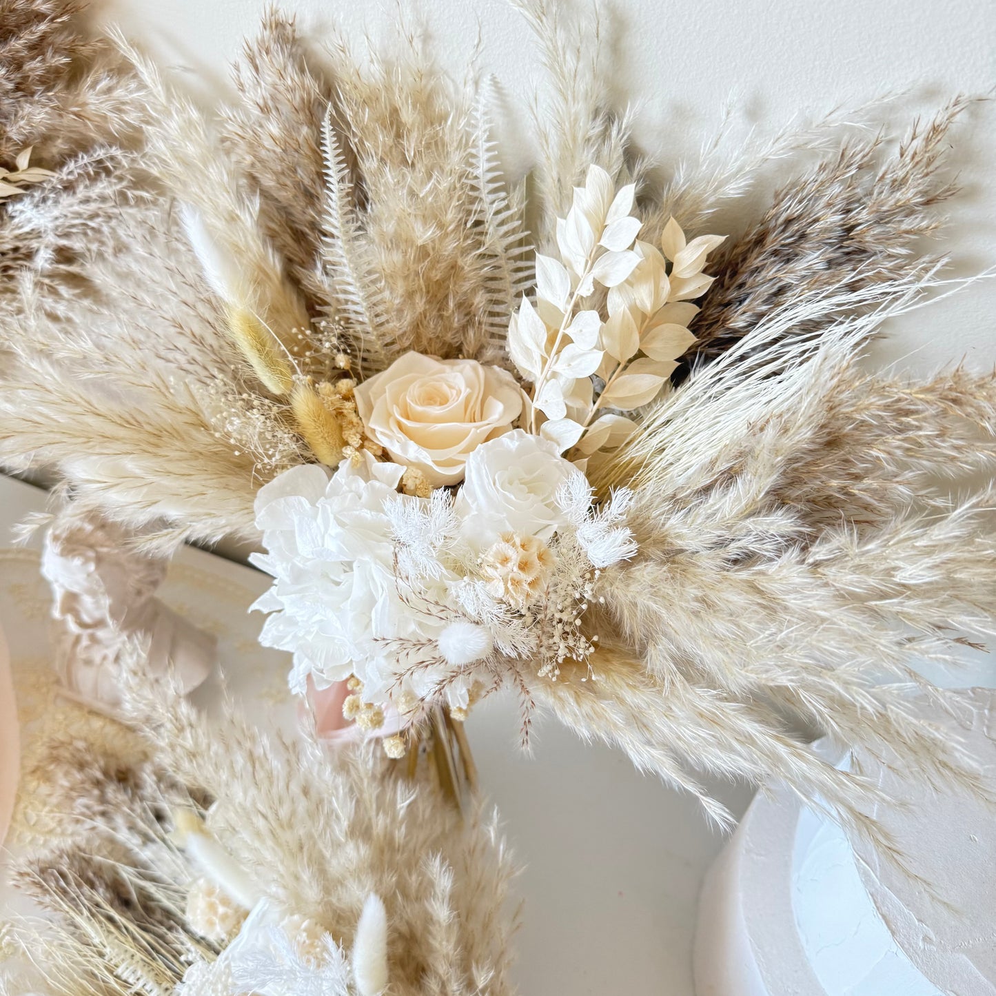 Decorative arrangement of dried pampas grass and flowers on a white surface