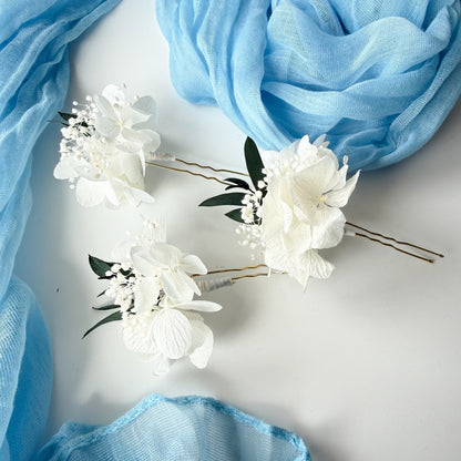 White floral hairpins with green leaves on a light gray background with blue fabric.