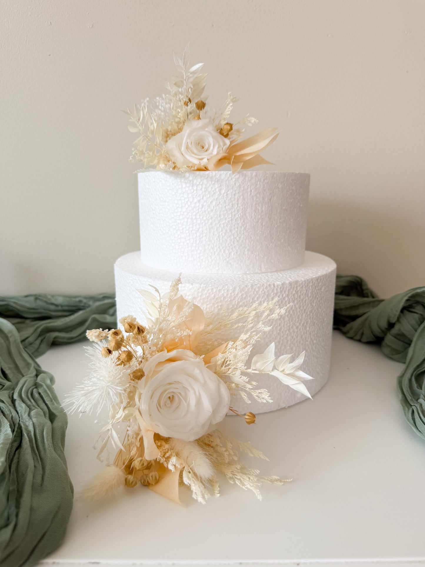 Two-tiered white wedding cake with floral decorations on a light background
